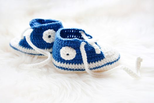 Little baby shoes. Handknitted first sneakers for newborn boy or girl. Crochet handmade bootees on fluffy white background.