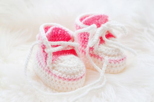 Little baby shoes. Hand knitted first sneakers for newborn girl. Crochet handmade pink bootees on fluffy white background.