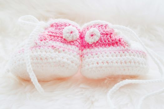 Little baby shoes. Hand knitted first sneakers for newborn girl. Crochet handmade pink bootees on fluffy white background.