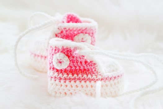 Little baby shoes. Hand knitted first sneakers for newborn girl. Crochet handmade pink bootees on fluffy white background.