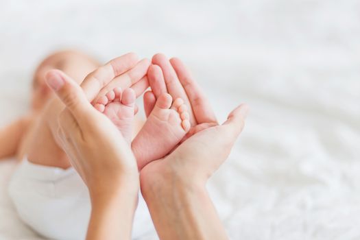 Mother holds newborn baby's bare feet. Tiny feet in woman's hand. Cozy morning at home.
