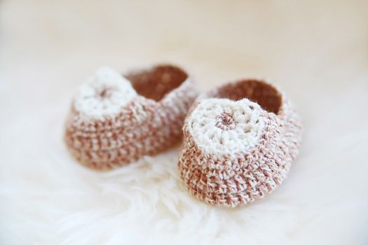 Little baby shoes. Hand knitted first bootees for newborn girl. Crochet handmade beige bootees on fluffy white background.