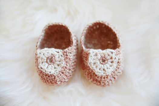 Little baby shoes. Hand knitted first bootees for newborn girl. Crochet handmade beige bootees on fluffy white background.