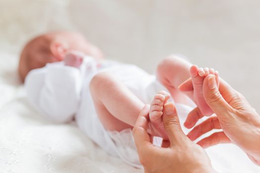 Mother holds newborn baby's bare heels. Tiny feet in woman's hand. Cozy morning at home.
