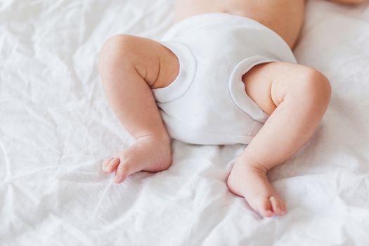 Baby's feet. Little child wearing white bodysuit and diaper. Cozy morning bedtime at home.