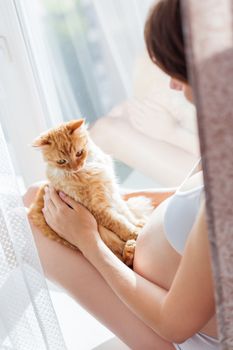 Pregnant woman in white underwear with cute ginger cat. Young woman expecting a baby. Risk of infection toxoplasmosis.