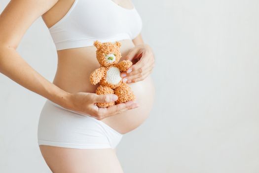 Pregnant woman in white underwear with toy bear. Young woman expecting a baby.