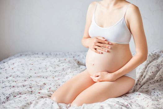 Pregnant woman in white underwear on bed. Young woman expecting a baby.