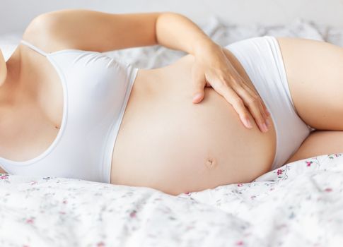 Pregnant woman in white underwear on bed. Young woman expecting a baby.
