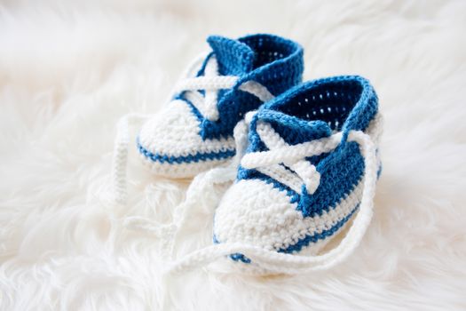 Little baby shoes. Handknitted first sneakers for newborn boy or girl. Crochet handmade bootees on fluffy white background.