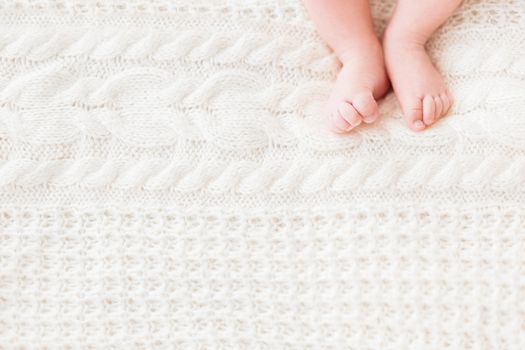 Baby's feet on white knitted background. Little child's bare feet. Cozy morning bedtime at home. Place for text.