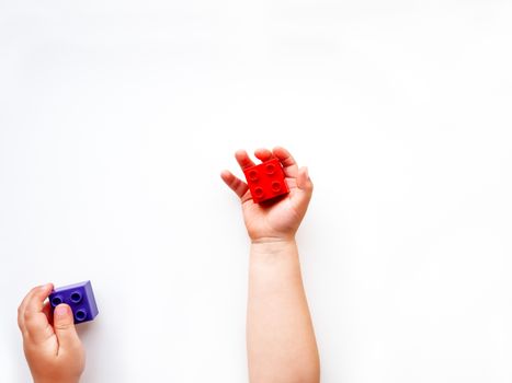 Child is holidng violet and red constructor blocks in fists. Kid's hands with toy on white background. Flat lay, top view.