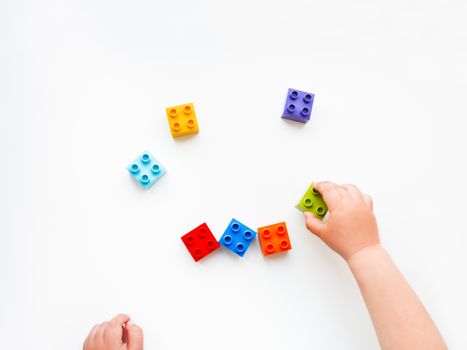 Child is playing with colorful constructor blocks. Kid's hands with bricks toy on white background. Educational toy, flat lay, top view.