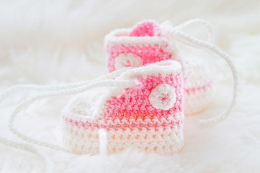 Little baby shoes. Hand knitted first sneakers for newborn girl. Crochet handmade pink bootees on fluffy white background.