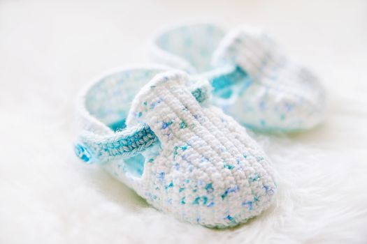 Little baby shoes. Handknitted first shoes for boy or girl. Crochet handmade bootees on white fluffy background.
