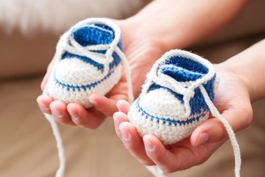 Little baby shoes. Handknitted first sneakers for boy or girl. Crochet handmade bootees in daddy's hands. Newly father presents knitted shoes.