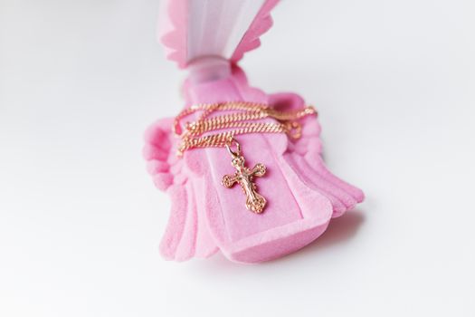 Golden cross for christening on pink gift box in shape of praying angel. Elegant religious accessory for little baby girl. Russian Orthodox church ceremony details.