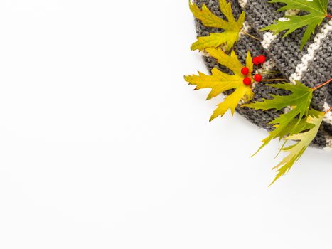 Grey knitted scarf with fallen leaves and berries on white background. Folded warm accessory with copy space.