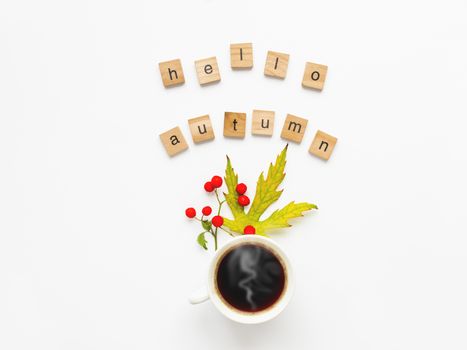 Cup of hot coffee with autumn leaves and berries on white background. Words HELLO AUTUMN. Warm beverage in white mug with copy space.
