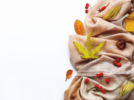 Beige scarf with fallen leaves and berries on white background. Folded warm accessory with copy space.