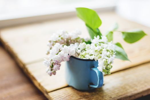 Lilac (Syringa) flowers in old rusty mug. Spring background with white and violet flowers in rustic cup on wooden table.