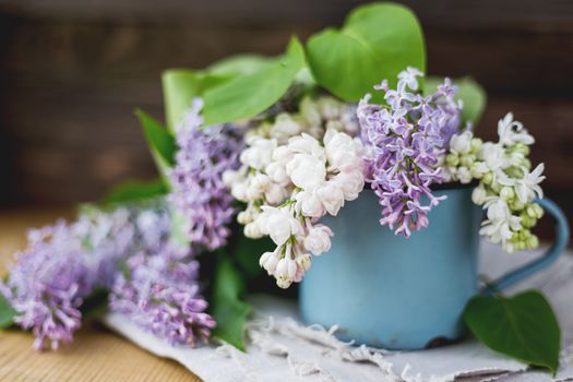 Lilac (Syringa) flowers in old rusty mug. Spring background with white and violet flowers in rustic cup on wooden table.