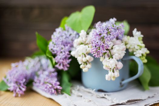 Lilac (Syringa) flowers in old rusty mug. Spring background with white and violet flowers in rustic cup on wooden table.