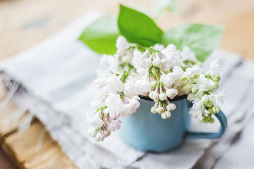Lilac (Syringa) flowers in old rusty mug. Spring background with white and violet flowers in rustic cup on wooden table.