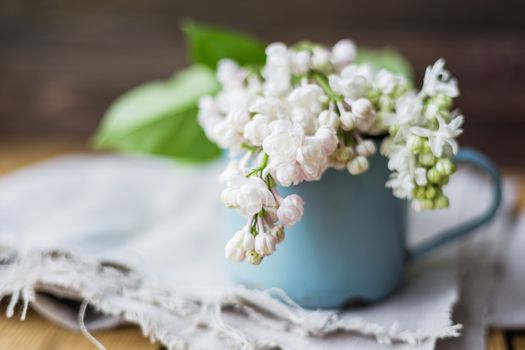 Lilac (Syringa) flowers in old rusty mug. Spring background with white and violet flowers in rustic cup on wooden table.