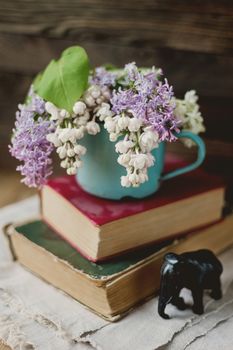 Two old books and rusty mug with lilac bouquet on homespun napkin. Statue of elephant. Interesting reading, vintage background.