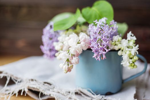 Lilac (Syringa) flowers in old rusty mug. Spring background with white and violet flowers in rustic cup on wooden table.