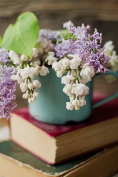 Two old books and rusty mug with lilac bouquet on homespun napkin. Interesting reading, vintage background.