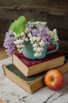 Two old books, apple and rusty mug with lilac bouquet on homespun napkin. Interesting reading, vintage background.