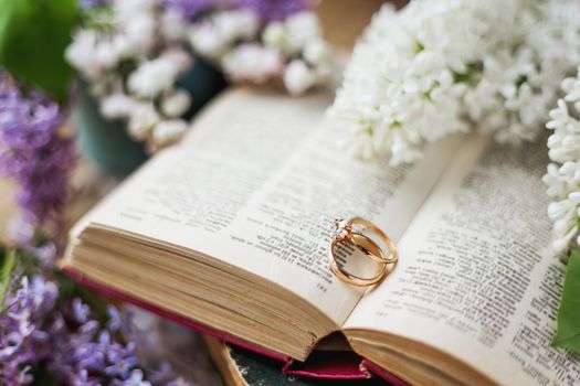 Pair of wedding rings with diamond. Rustic background with old books and lilac flowers. Retro background.