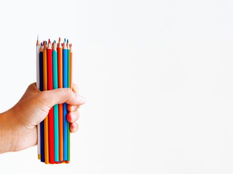 Hand with bunch of colorful pencils on white background. School supplies on white background. Kid's stationery. Back to school copy space backdrop.