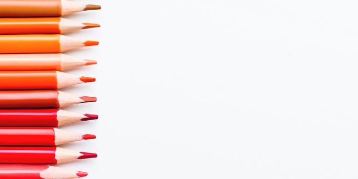Row of colorful red and orange pencils on white background. School supplies on blackboard. Kid's stationery. Back to school copy space backdrop.