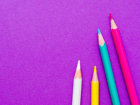 Row of colorful watercolor pencils on lilac background. School supplies on purple paper background. Kid's stationery. Back to school magenta backdrop.