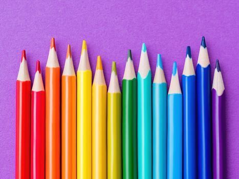 Row of colorful watercolor pencils on lilac background. School supplies on purple paper background. Kid's stationery. Back to school magenta backdrop.