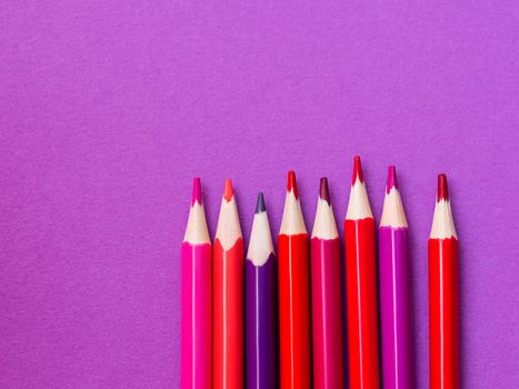 Vertical row of red and magenta pencils on purple paper background. School supplies. Kid's stationery with lilac copy space. Back to school pink backdrop.