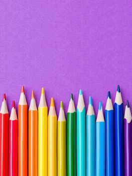 Row of colorful watercolor pencils on lilac background. School supplies on purple paper background. Kid's stationery. Back to school magenta backdrop.
