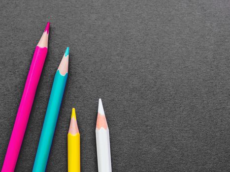 Row of colorful watercolor pencils on dark grey paper background. School supplies on blackboard. Kid's stationery. Back to school black backdrop.