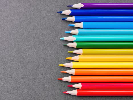 Horizontal row of colorful pencils on grey paper background. School supplies in colores of rainbow on blackboard. Kid's stationery with black copy space. Back to school backdrop.