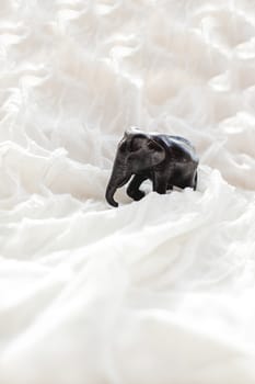White textile background with elephant figure. Small asian souvenir on fabric with ruches.