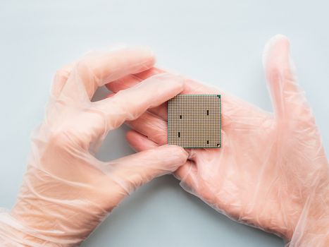 Hands in rubber glove with Central Computer Processor. CPU on light blue background. Technological detail of personal computer.