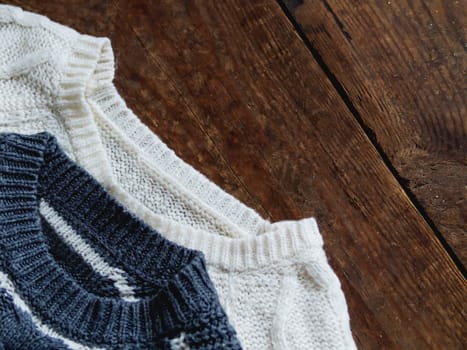 Grey and white knitted sweaters on shabby wooden background. Top view, flat lay.