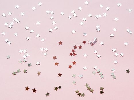 Holiday background with silver star confetti on pink background. Good backdrop for Christmas and New Year cards. Flat lay, top view.