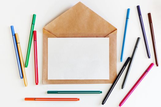 Clear sheet of paper on craft envelope. Background with colorful pens. Mock up. Flat lay, top view.