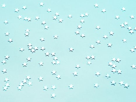 Holiday background with silver star confetti on aquamarine background. Flat lay, top view.