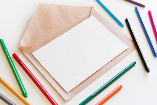 Blank sheet of paper on craft envelope. Background with colorful pens. May be used as mock up.