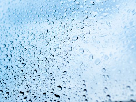 Rain drops on glass. Silhouettes of light blue water drops on a transparent surface.